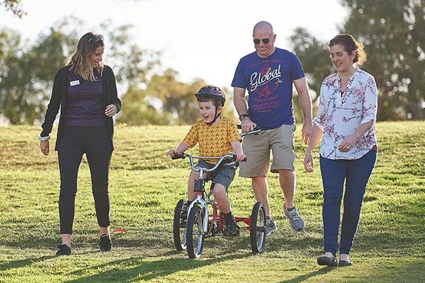 Boy riding bike with his parents and therapist