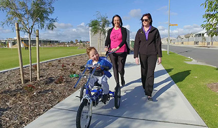 Theodore rides his bike and is accompanied by mum Sharon and his therapist next to a park.