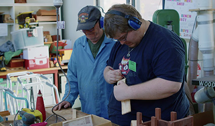 Young man doing woodwork with older man at Men's Shed