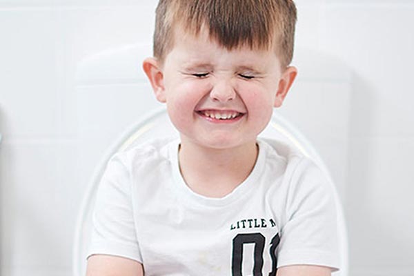 Boy sits on toilet with eyes closed holding book