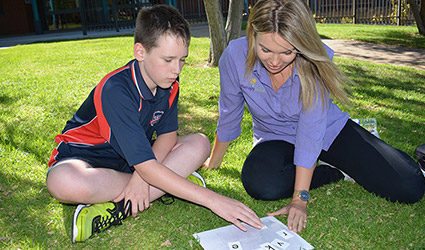 A boy and therapist sit together on some grass. They interact with a therapy resource.