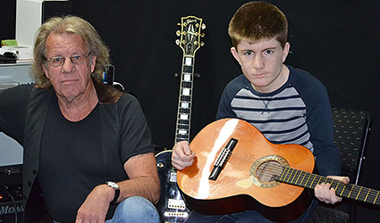 Boy holding guitar sitting next to teacher