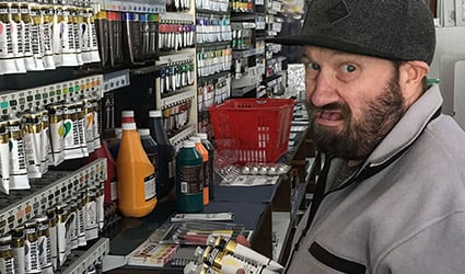 Man with hat on putting away paints at art shop