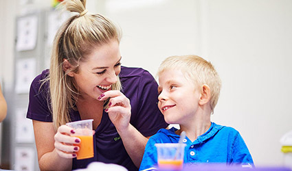 Therapist holds drink and laughs with young boy