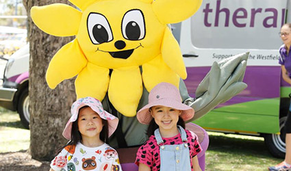 Two young children smile infront of Therapy Focus mascot.