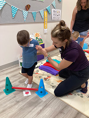 A young boy stepping over a small hurdle with help from Katherine