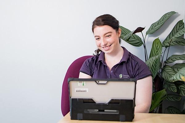 A therapist smiles at computer screen during a teletherapy session