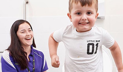 Boy and continence clinician laughing in bathroom receiving bedwetting support