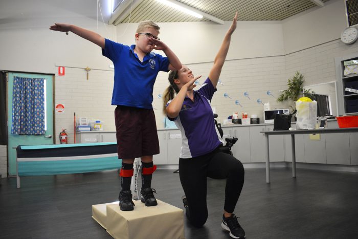boy stands on step and celebrates with therapist