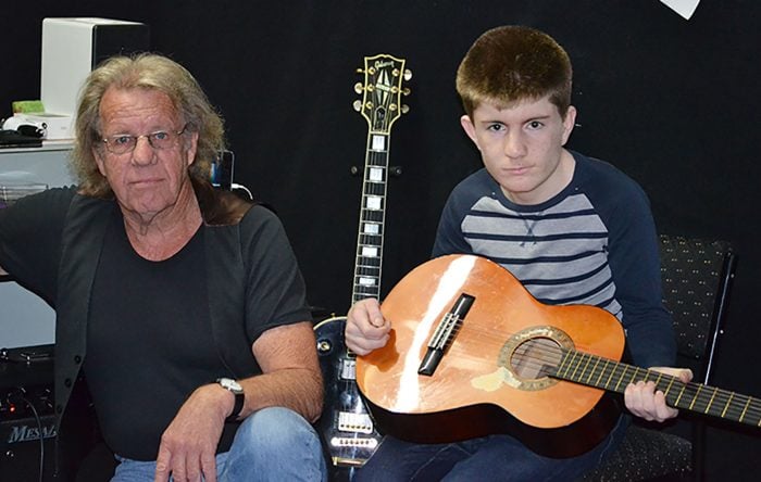 Boy holding guitar sitting next to teacher