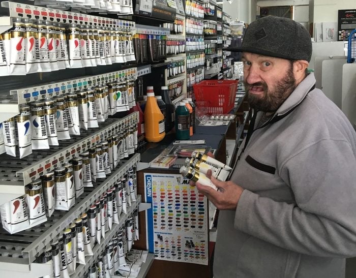man with hat on putting away paints at art shop