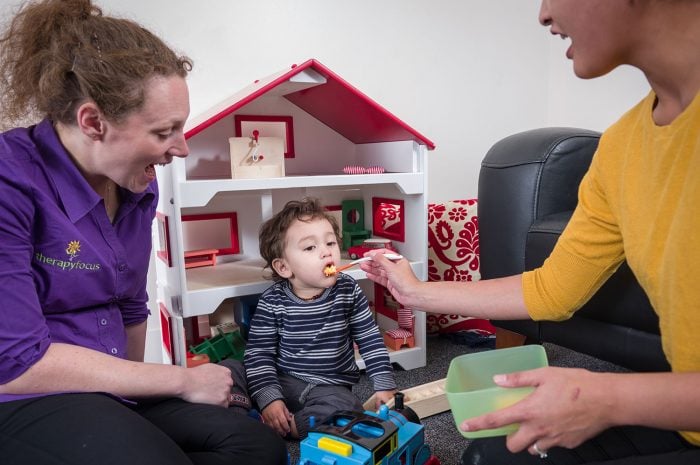 mother feeds child with therapist looking on