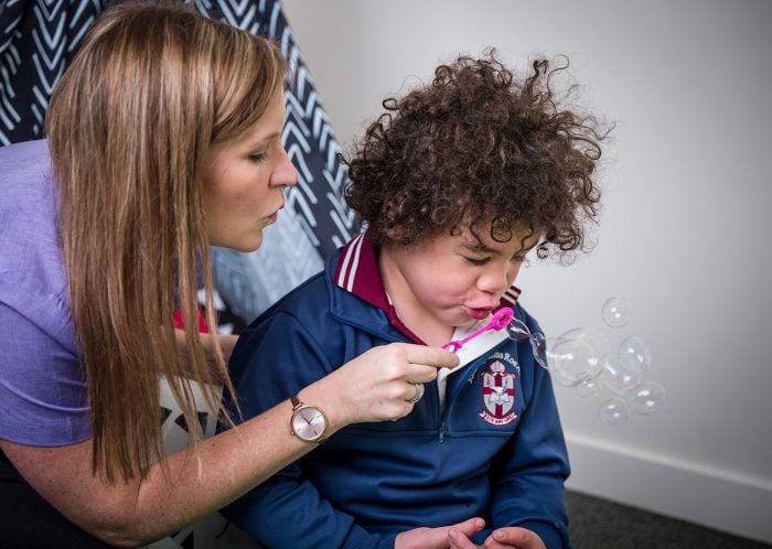 child blows bubbles with help of therapist