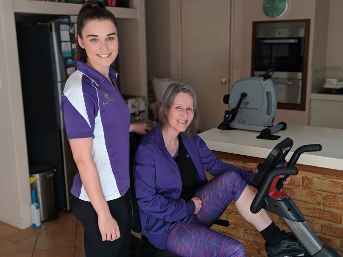 Therapist and a mature woman on an exercise bike smiling