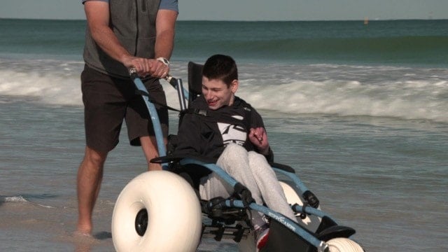 Harrison being pushed on the beach in his beach wheelchair