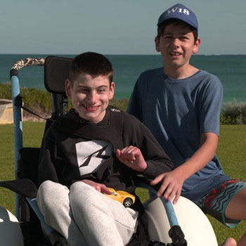 Harrison in his beach wheelchair with his brother knelt beside him