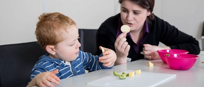 A child inspecting some food as a therapist looks on