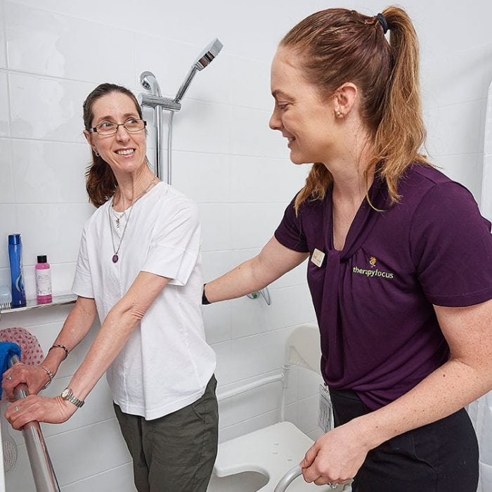 Therapist supports client holding shower rail in bathroom