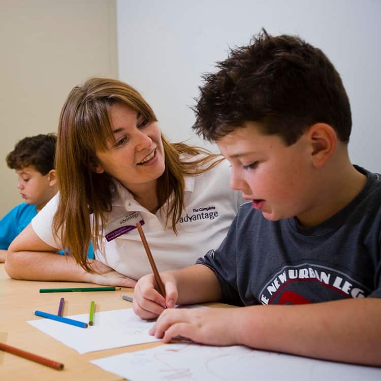 Therapist talks to young boy as he draws a picture