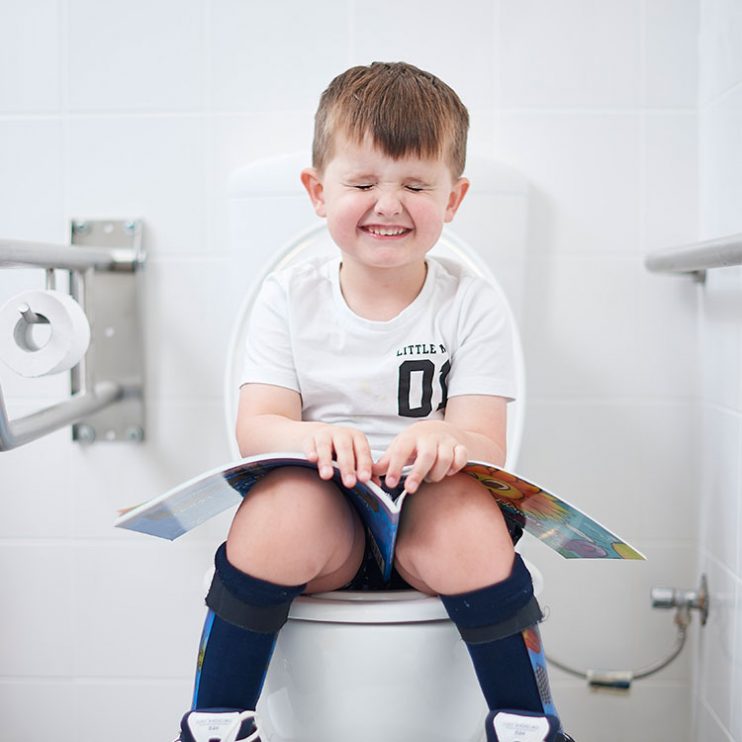 Boy sits on toilet with eyes closed holding book