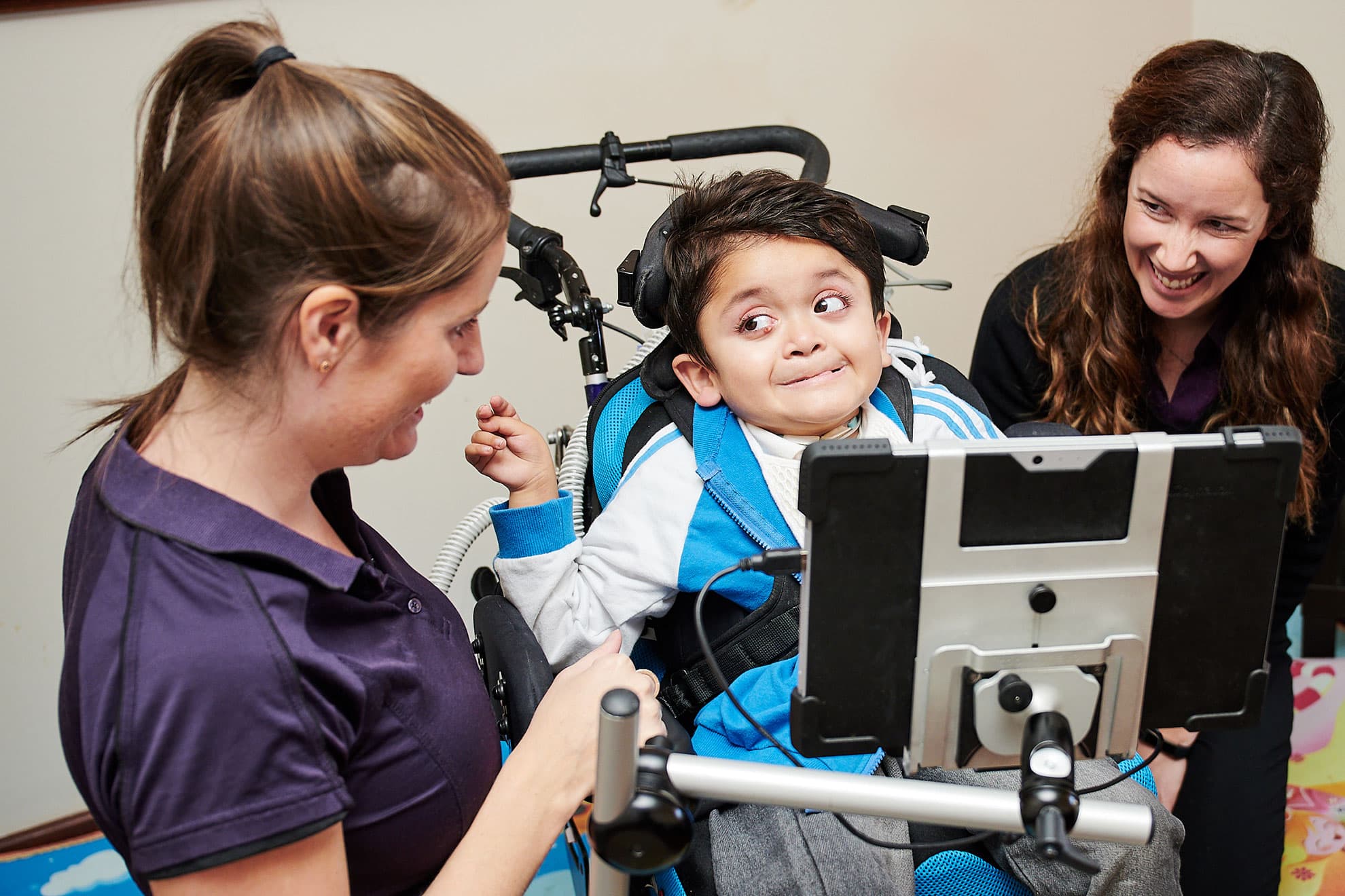 A boy in a wheelchair looking at a therapist with the support of assistive technology