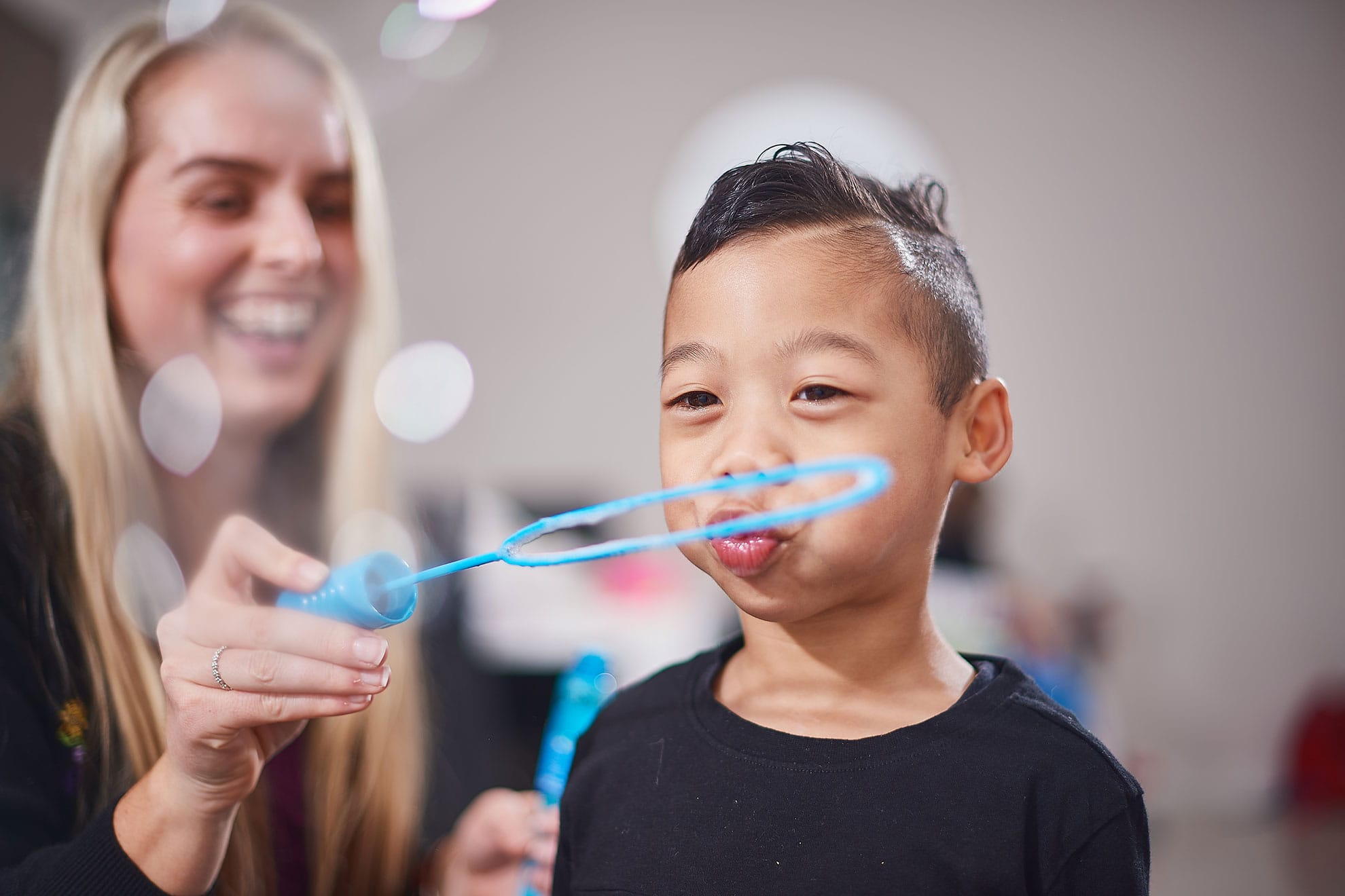 A boy blowing bubbles with a therapist smiling in the background