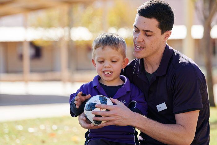 A physiotherapist handing a ball to a boy with dwarfism