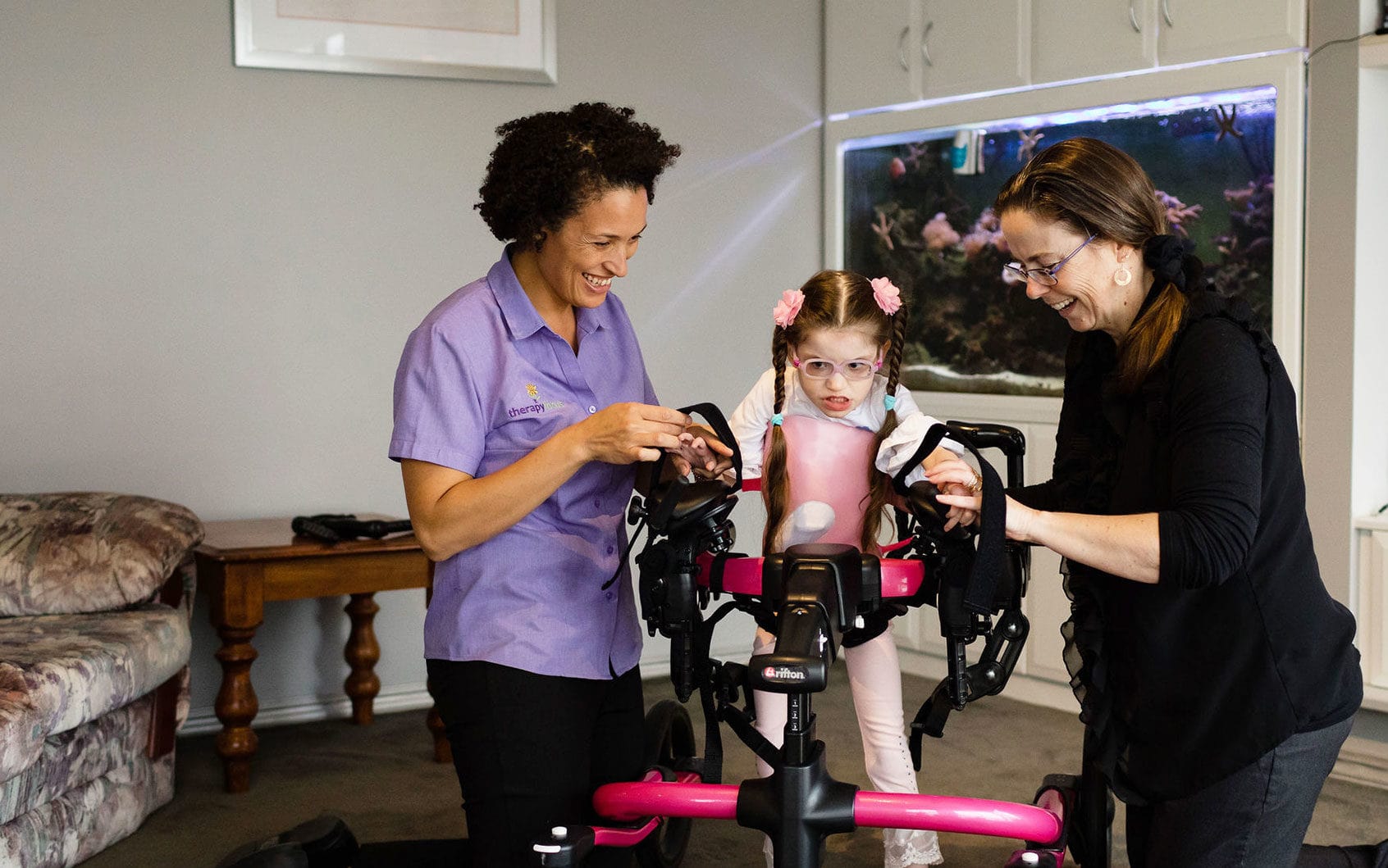 A young girl in a walker with her Mum and therapist