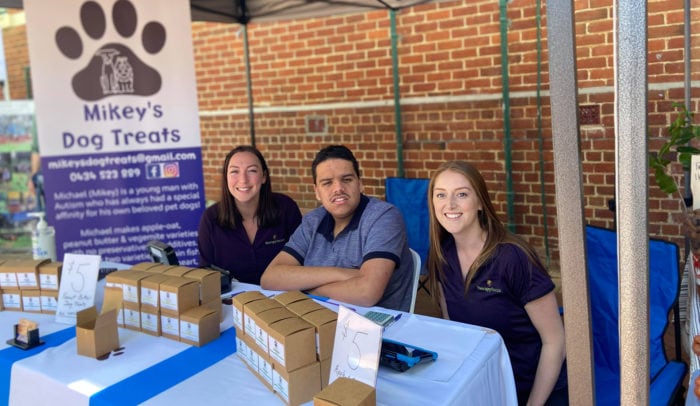 Mickey sits at his dog treat stall with two Therapy Focus therapists.