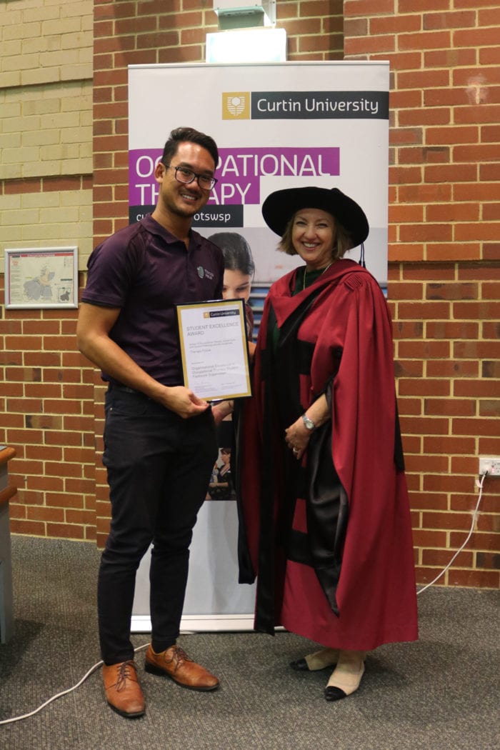 Joshua Panelo (left) stands with Marina Ciccarelli (right) and smiles. Joshua is holding the award. 