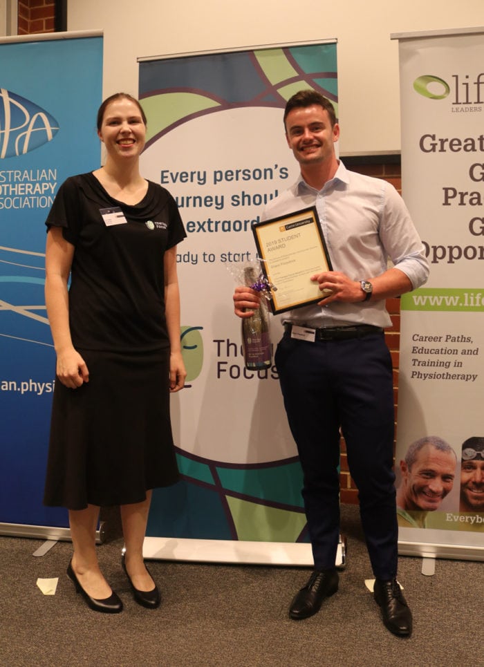 Lucie Abadi (left) and Shaun Fitzpatrick (right) pose together and smile. Shaun holds his award. 