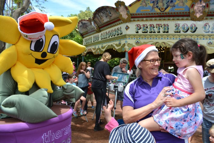 Sunny the sunflower says hello to a customer and therapist in front of the Perth Zoo Carousel