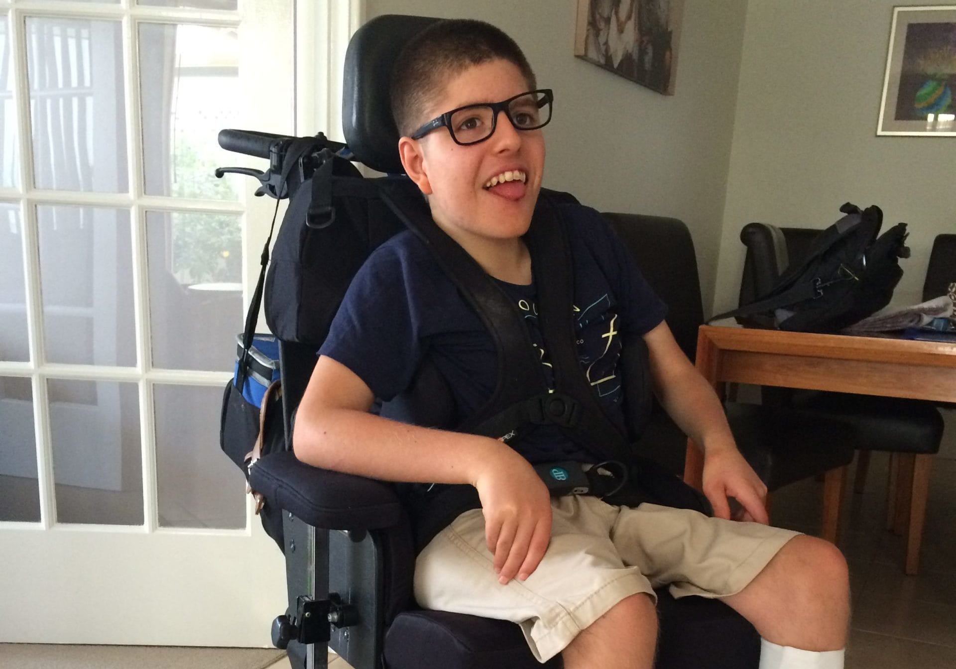 Harrison uses his wheelchair and smiles.