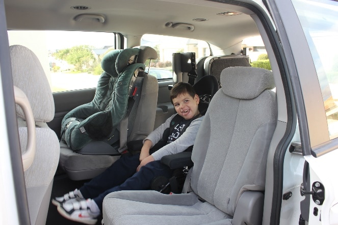 Noah sits in his car seat in the car. He is smiling at the camera. The car has a grey interior.