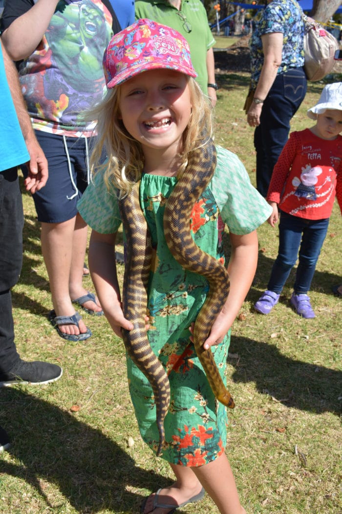 A young girl smiles with a snake around her neck.