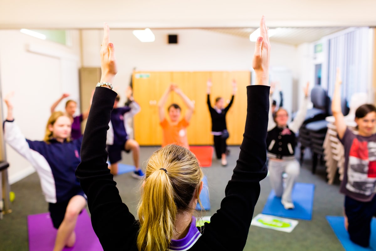 Students and therapist engage in Yoga. They stand on mats with their arms raised in the air.