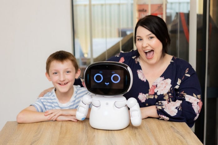 A customer and his mum smile while sitting with a social robot