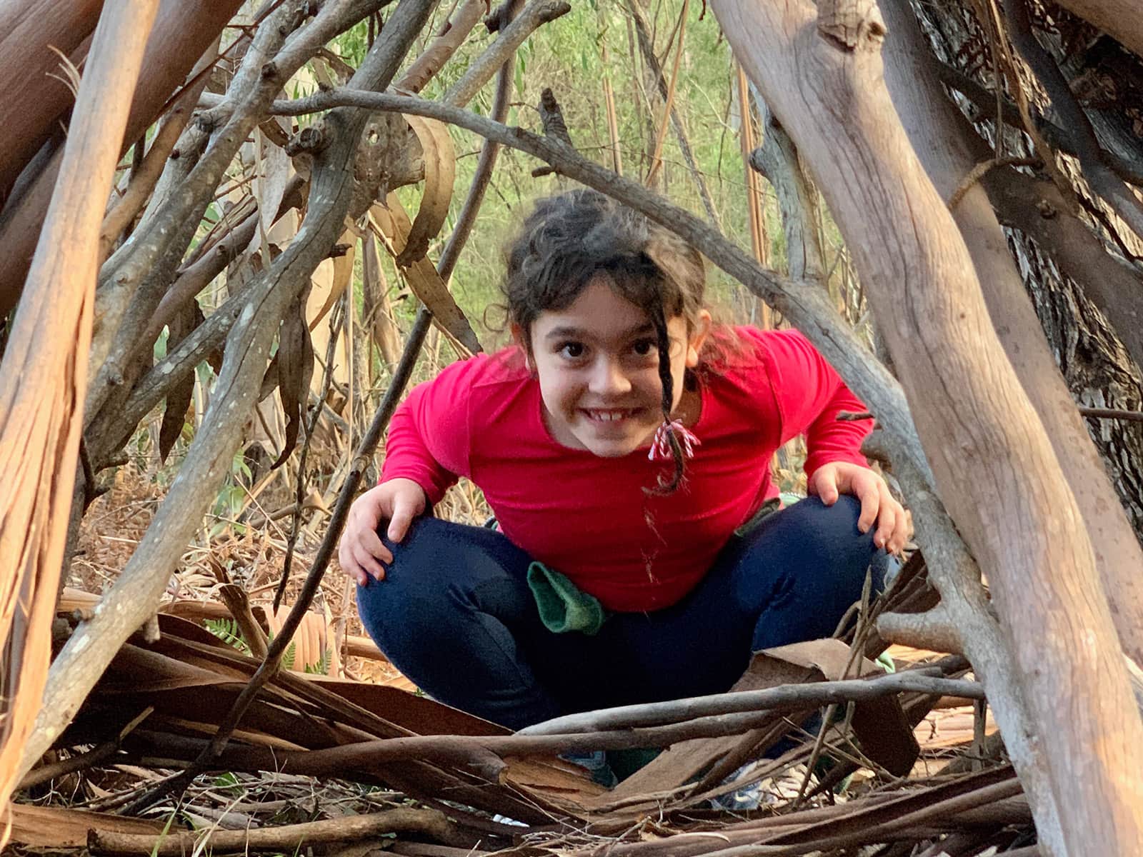 Young girl crouches and smiles as she looks through some trees