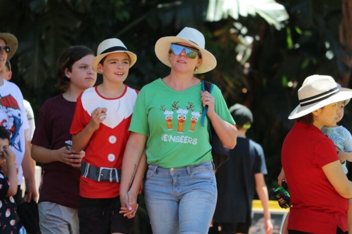 2 Customers are walking. One is wearing a green top and hat and the other is wearing a red santa top and hat.