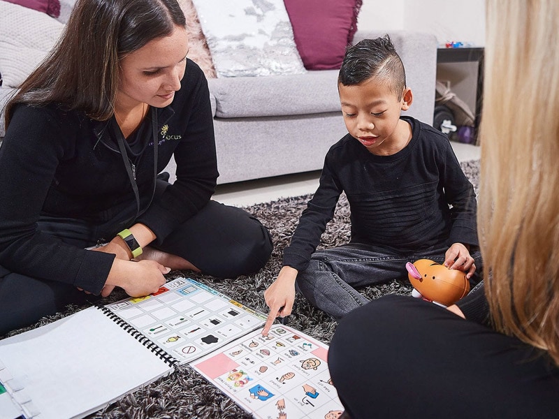 Two therapists and a young boy sit on the floor during a positive behaviour support session.