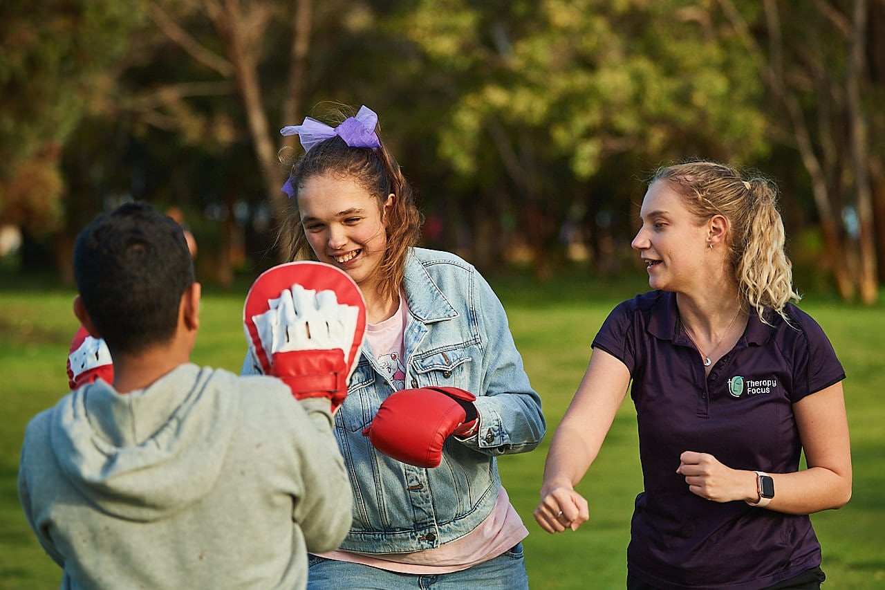 Physiotherapists and two teenagers do boxing exercises in a park.