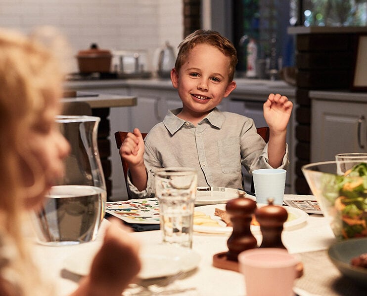 Ethan sits at the dinning table with his family and smiles at the camera. He is wearing a collared shirt.