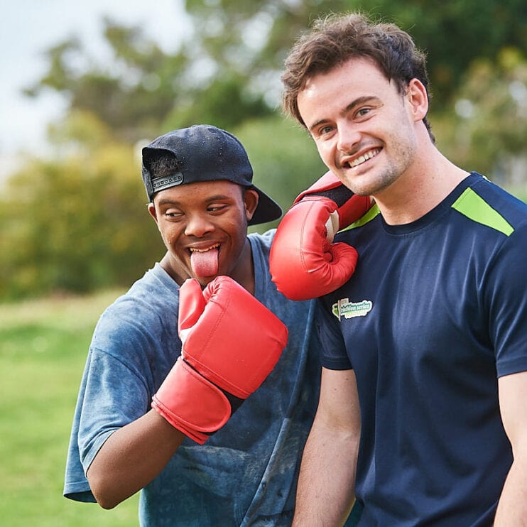 Physiotherapists and a teenager outdoors. The teenager is wearing boxing gloves and has his tongue out.