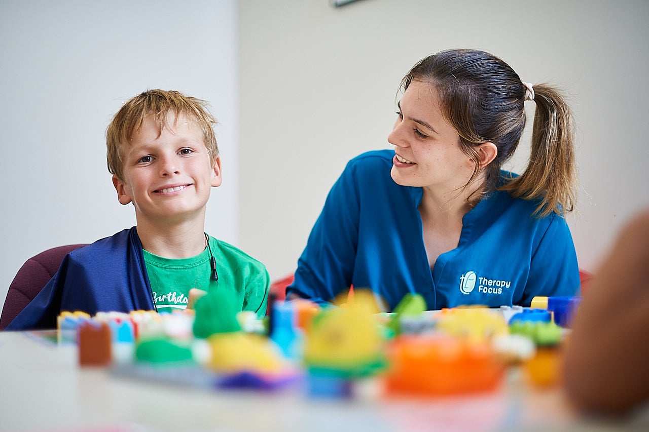 Female therapist talking to young boy while playing with logo blocks