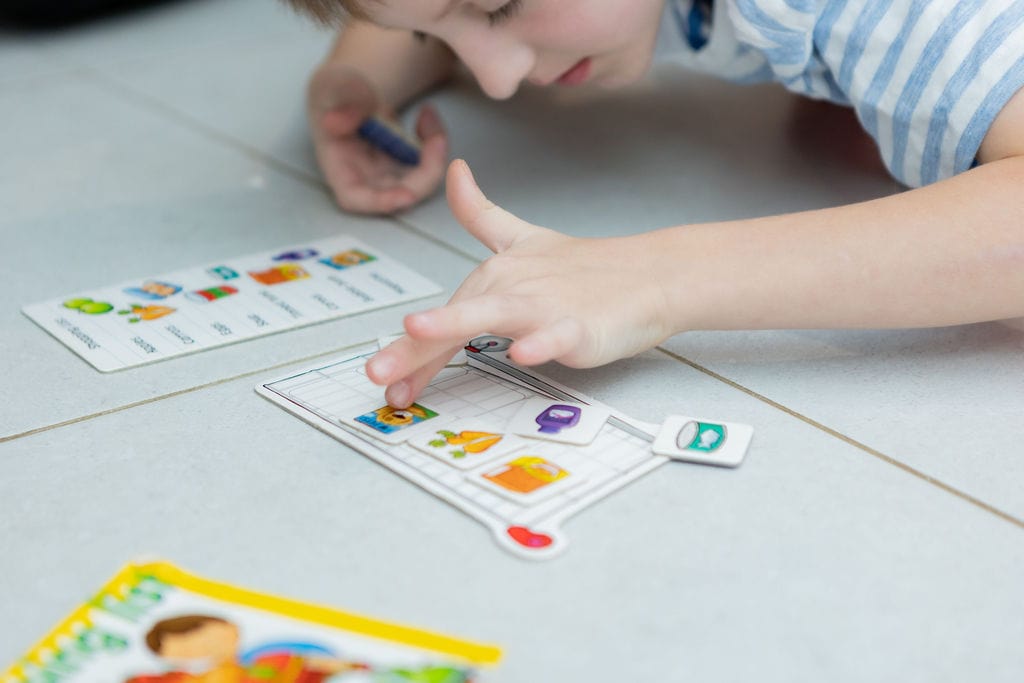 A young boy lays on the floor and plays with an activity. He sticks stickers to a piece of paper. 