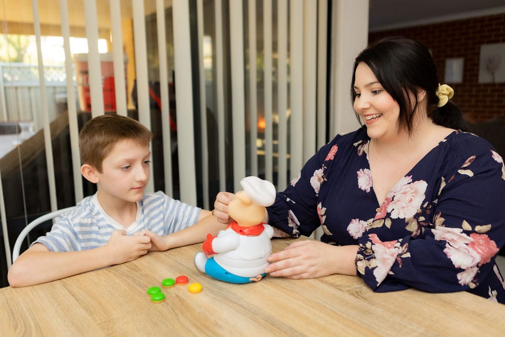 A young boy and his mother engage in an activity together. They sit at a dining room table. 