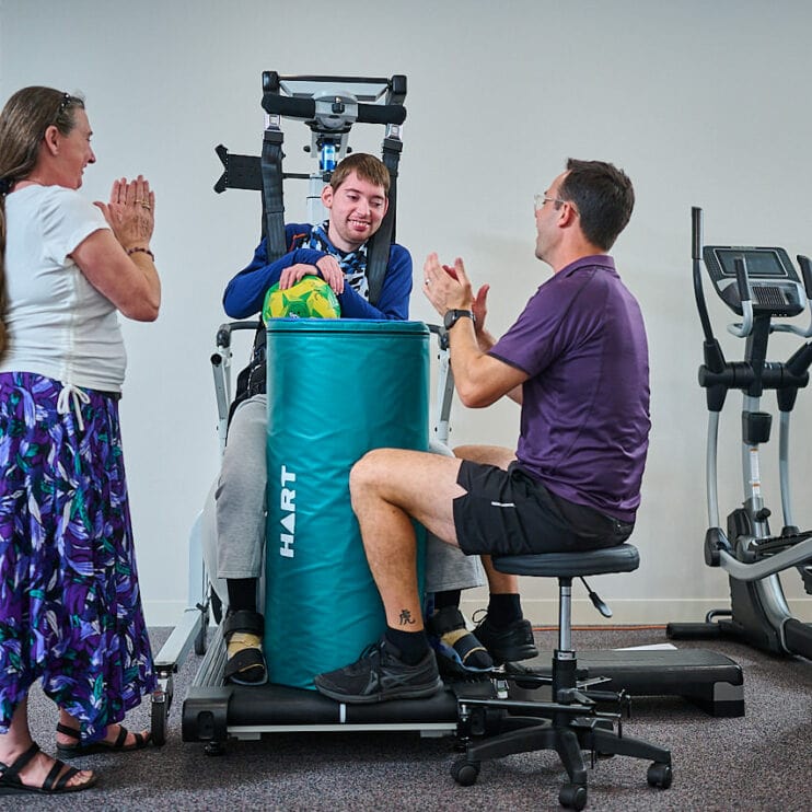 A young man using a Litegait machine with his therapist and parent watching
