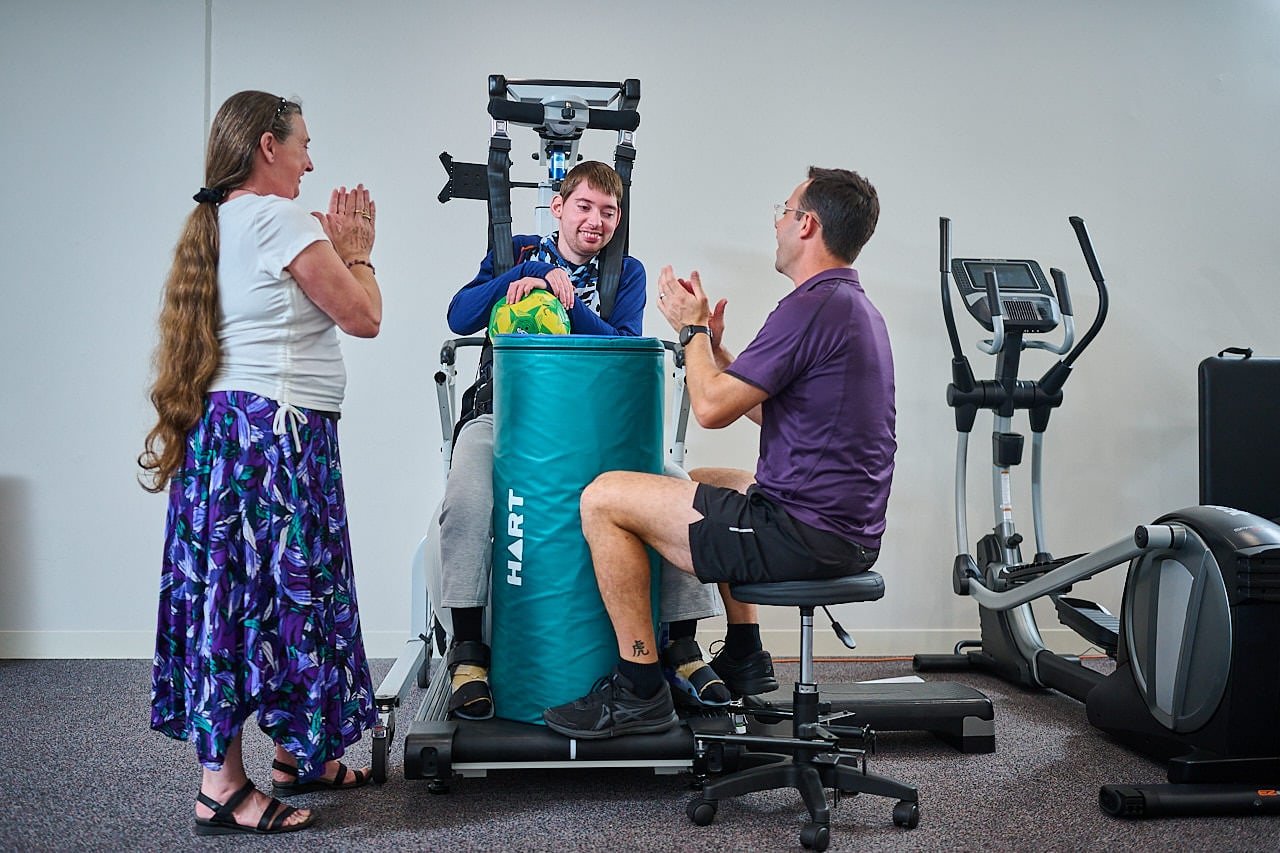 A young man using a Litegait machine with his therapist and parent watching