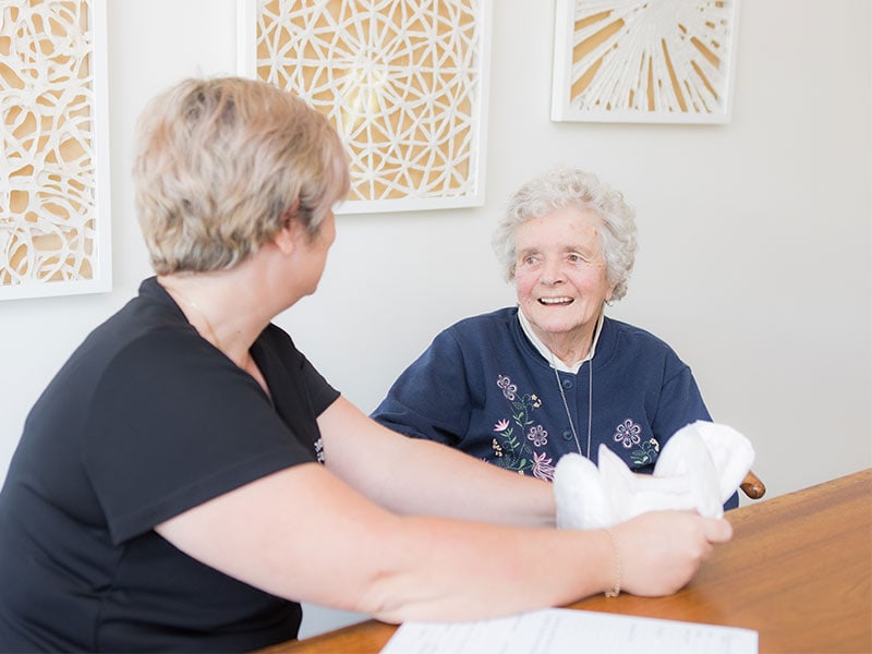 An elderly lady smiling at a nurse holding a pad