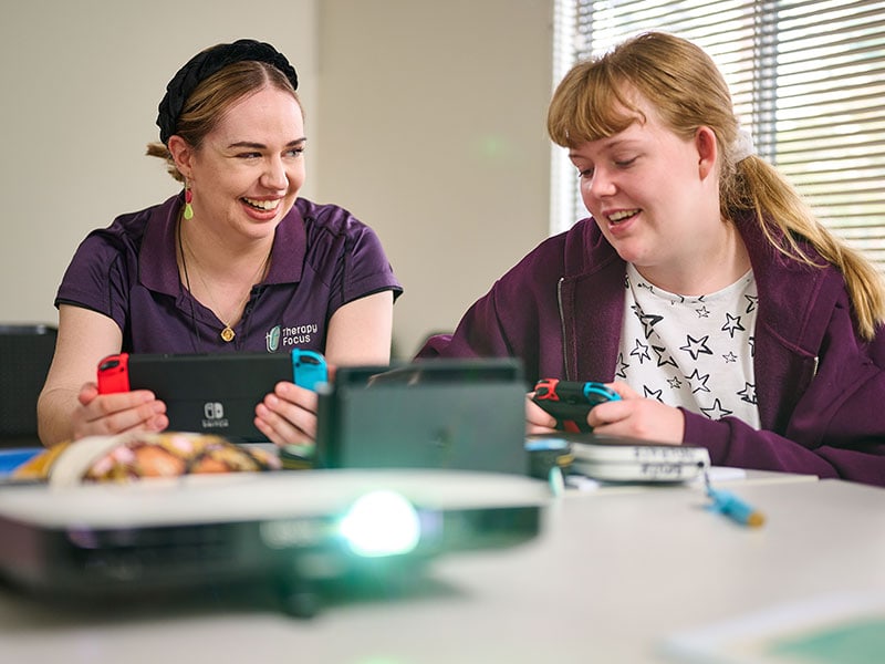 A therapist and teenage girl holding game consoles